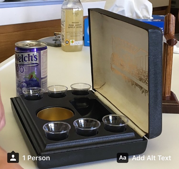 An open portable communion set on a table, with small cups and a bottle of grape juice beside it.